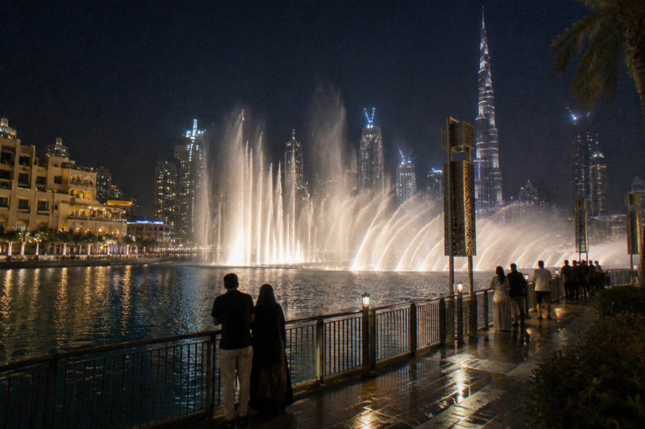 Water fountains rising over a lake between tall buildings in the evening