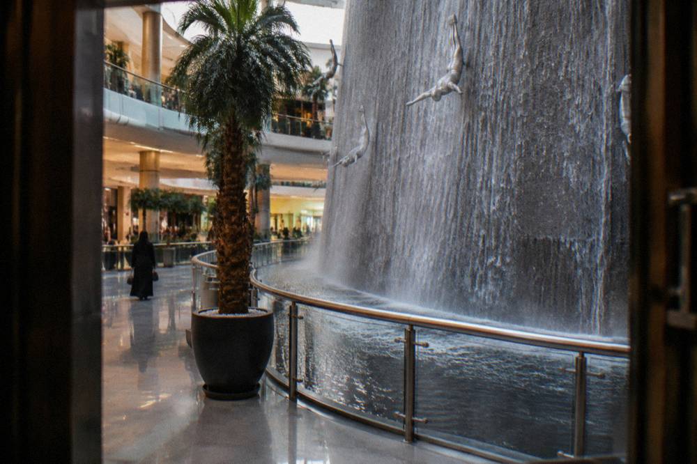 Open air corridor of a large Dubai shopping mall with a tall indoor waterfall structure
