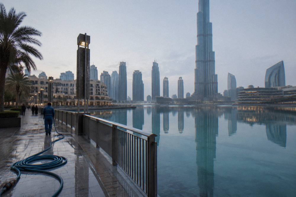 The Dubai Fountain lake and surrounding towers seen from a public waterfront promenade