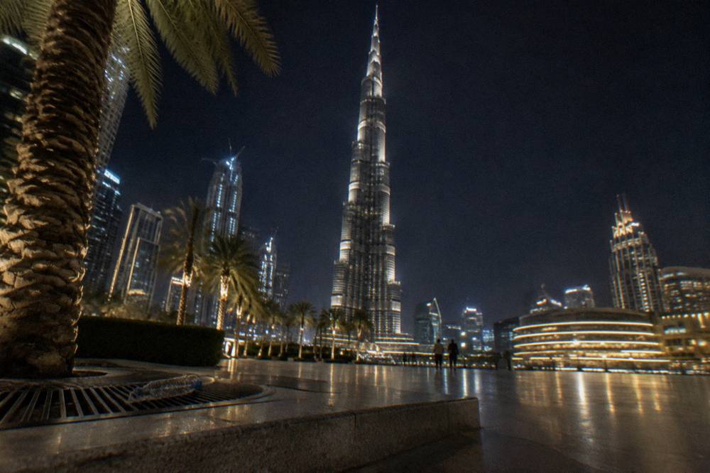 The Burj Khalifa tower lit up against the night sky above the Downtown Dubai plazas