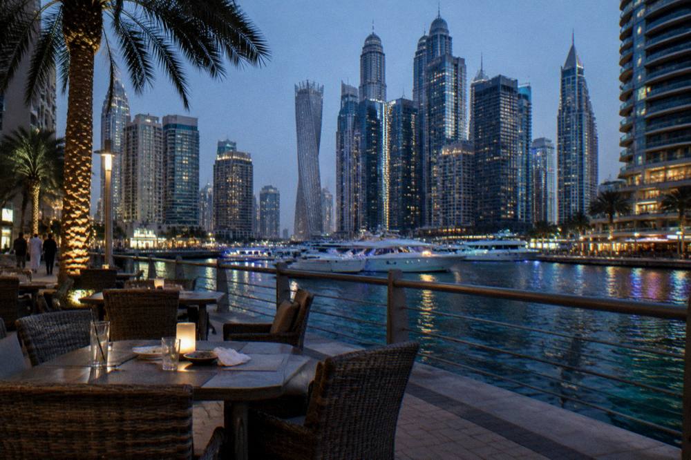 Outdoor waterfront dining area with tables along a promenade at dusk