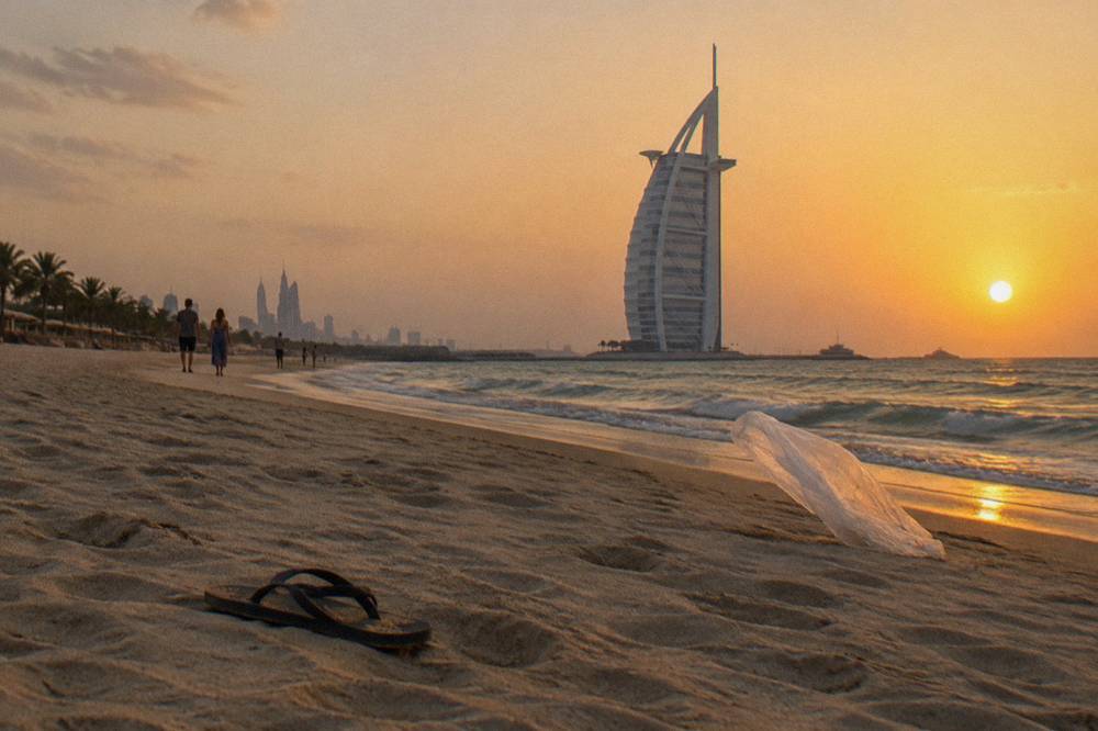 A sandy beach with a tall sail-shaped hotel tower in the distance