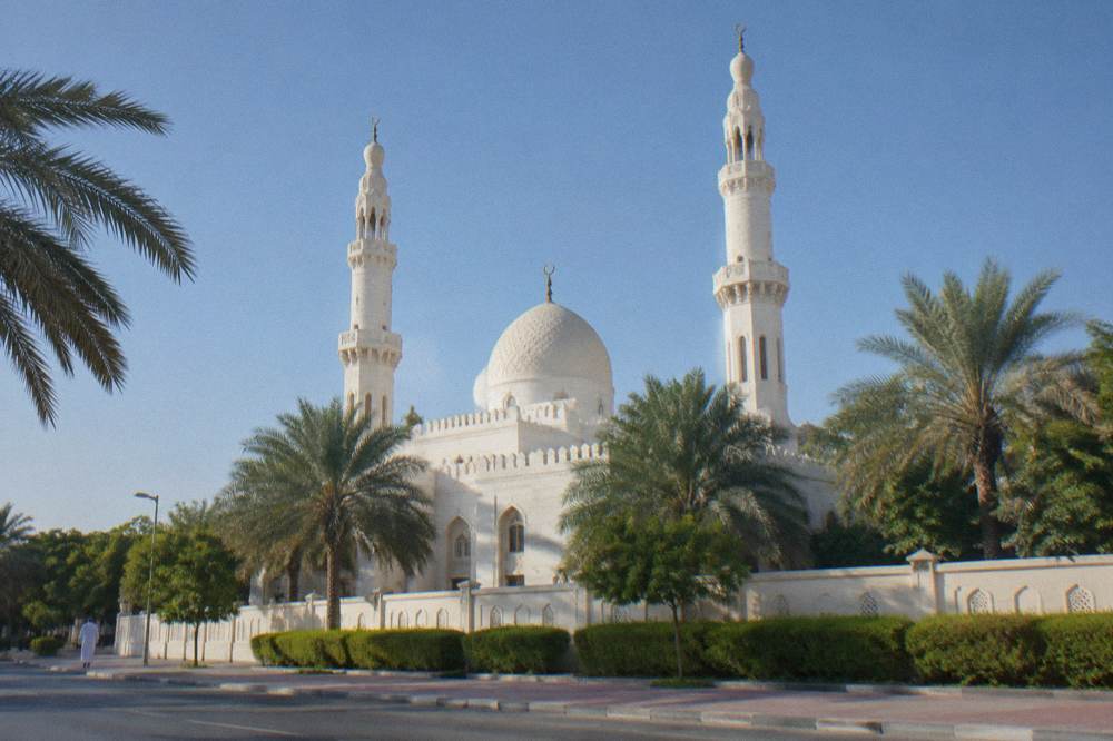 A white mosque with a large dome and two minarets under a clear sky