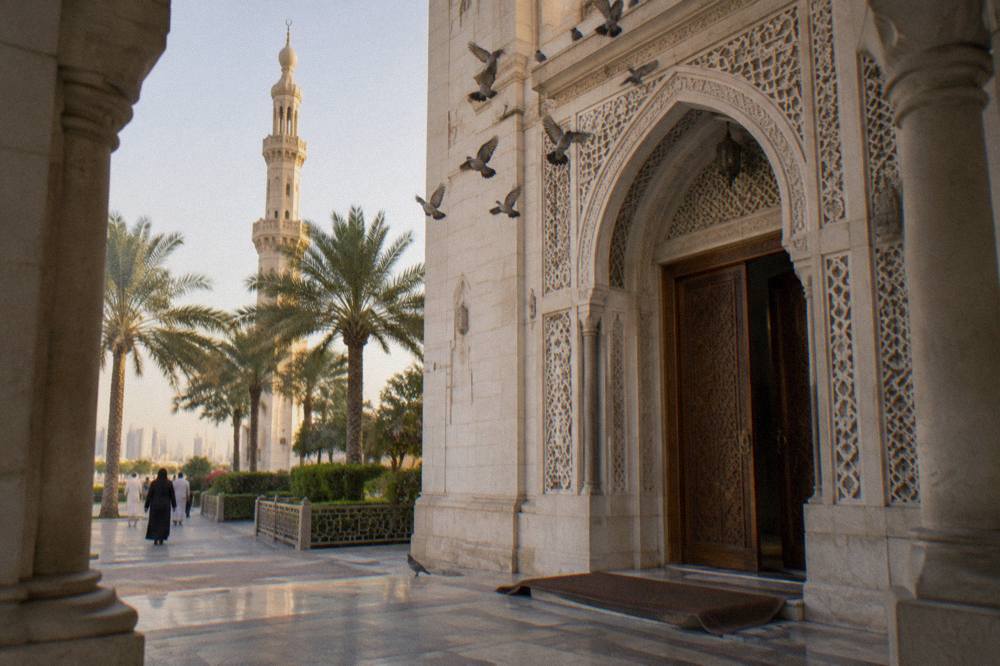 Arched entrance of a white stone mosque with carved wooden doors