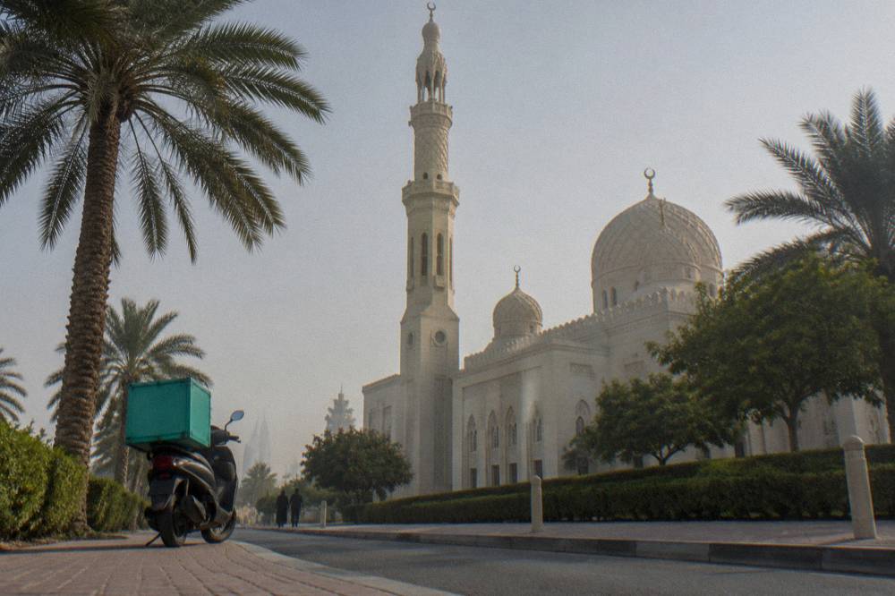 Tall white minaret rising above a mosque roofline against open sky