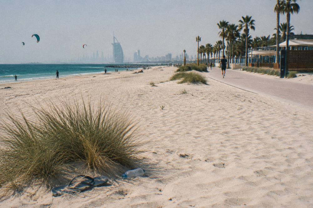 bright midday beach with open sand and a long waterfront path
